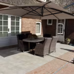 Terras met rotan tuinset, parasol en Kera Full Body tegels naast klinkerrand