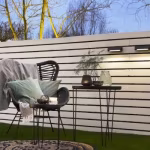 Witte horizontale schutting met Wedge Slim wandlampen naast rotan stoel en bijzettafel