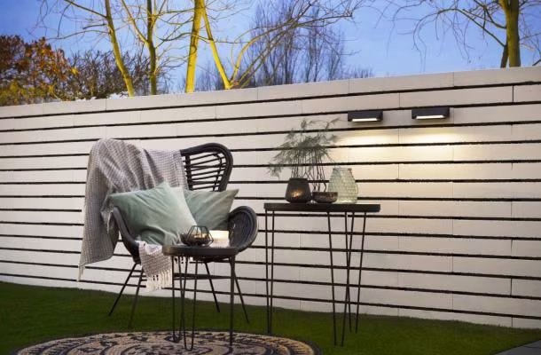 Witte horizontale schutting met Wedge Slim wandlampen naast rotan stoel en bijzettafel