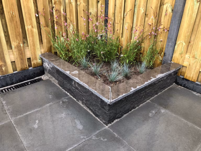 Hoekige plantenbak van antraciet Wallblock Split 10x10x40 voor houten schutting met siergras