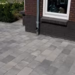 Terras van Tambour Smook bestrating langs bakstenen woning met regenpijp