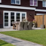 Tuin met gazon, pad en terras van Tambour Smook bestrating bij bakstenen woning