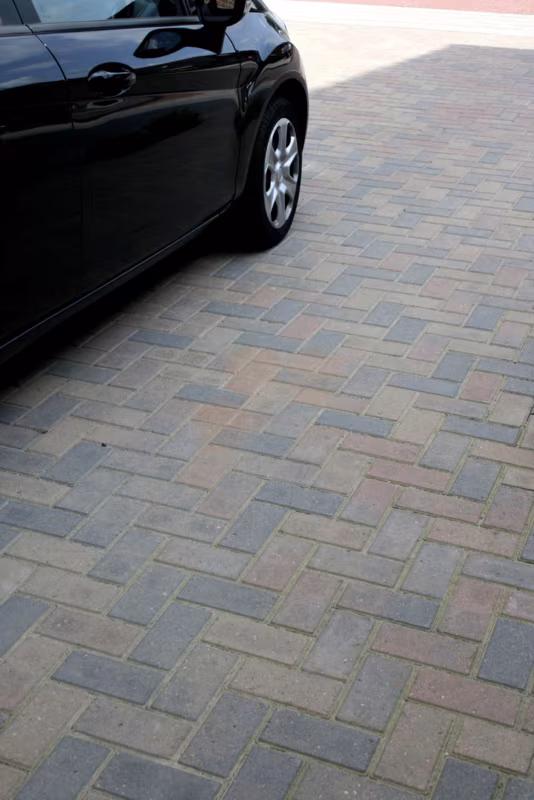 Oprit met Tremico BKK bont klinkers in grijsbruin patroon naast zwarte auto