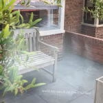 Terras met houten bank en bakstenen muur, tekst Kera Full Body Leuven 60x60x3 cm