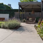 Tuinpad van lichtgrijze terrastegels langs lavendel naar overkapping met loungeset