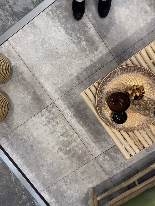 Bovenaanzicht Soft Comfort Grezzo tegels met schaal op bamboe tafel en voeten van persoon