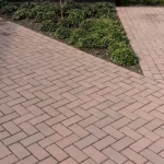 Oprit van roodbruine klinkers in visgraatverband langs plantvak met struiken en zwarte randafwerking
