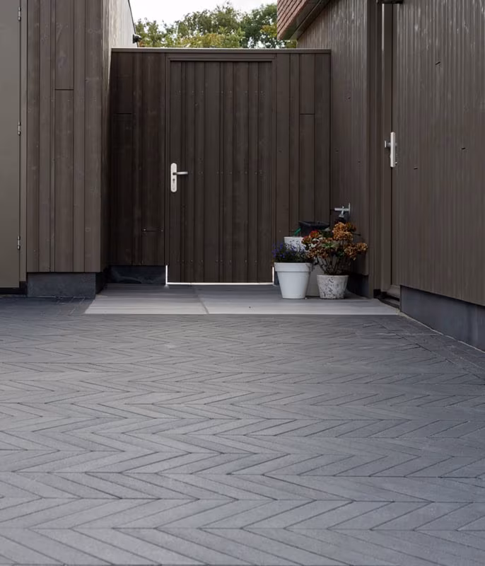 Donkergrijze visgraatbestrating voor een houten tuindeur met bloempotten
