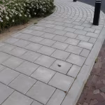 Gebogen voetpad van grijze betontegels langs bloemenborder en zwarte paaltjes