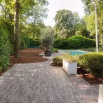 Kronkelend tuinpad van Lotis getrommelde klinkers langs witte plantenbakken tussen bomen