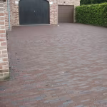 Brede oprit van rode en bruine klinkers voor twee garagedeuren met bakstenen muur