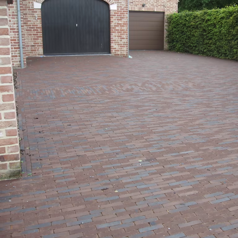 Brede oprit van rode en bruine klinkers voor twee garagedeuren met bakstenen muur