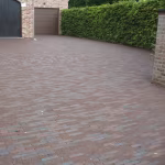 Oprit met rode en bruine klinkers voor garages met bakstenen gevel en haag