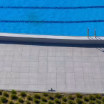 Zwembadrand met GeoCeramica Fiordi Sand tegels, blauw water en lage struiken