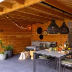 Houten overkapping met eettafel, hanglampen en loungebank op GeoCeramica Flow Black tegels