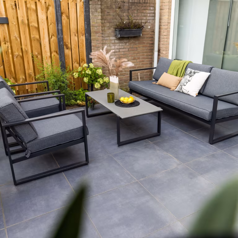 Loungeset met salontafel en pampasgras op GeoCeramica Flow Black tegels bij houten schutting