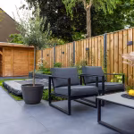 Zwarte loungestoelen en olijfboom in pot op GeoCeramica Flow Black tegels langs schutting