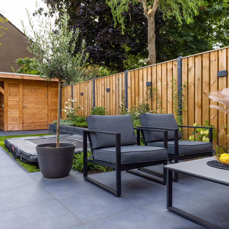Zwarte loungestoelen en olijfboom in pot op GeoCeramica Flow Black tegels langs schutting