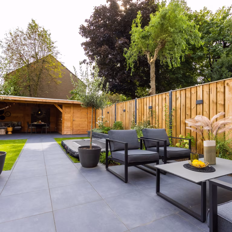 Tuin met GeoCeramica Flow Black tegels, zwarte loungestoelen, salontafel en houten schutting