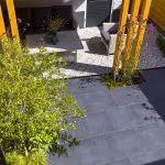 GeoCeramica Flow Black tegels naast overkapping met gele houten palen en loungeset