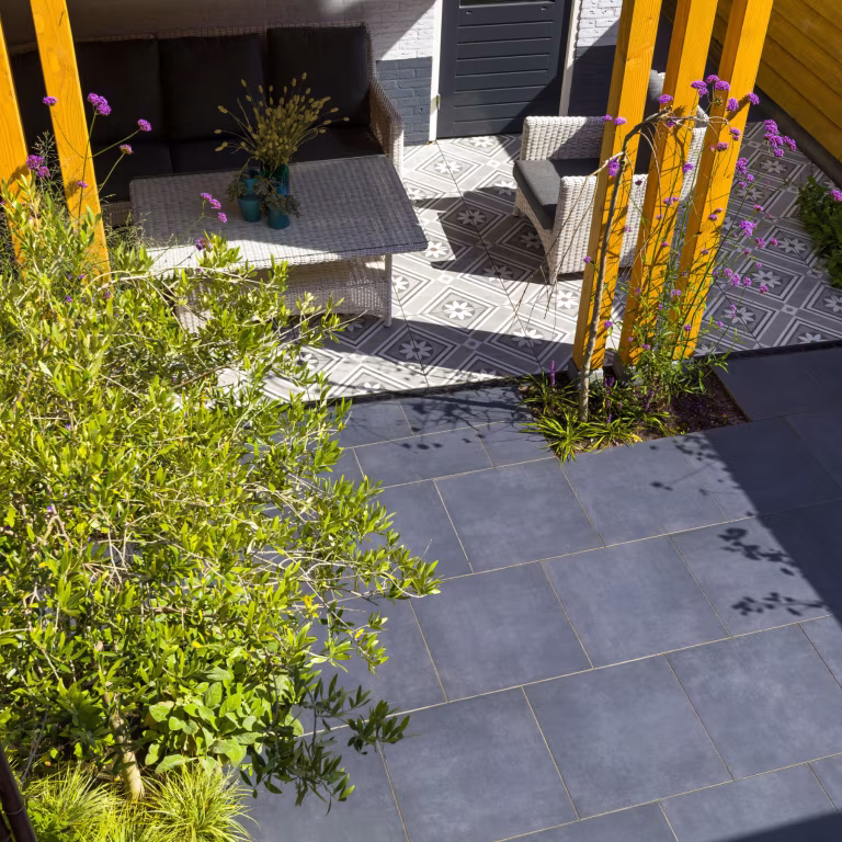 GeoCeramica Flow Black tegels naast overkapping met gele houten palen en loungeset