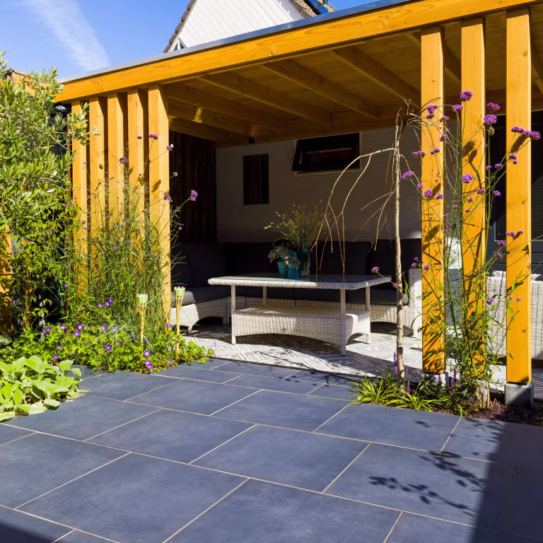 Open overkapping met gele houten balken en loungehoek op GeoCeramica Flow Black tegels