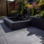 Vijver met zwarte rand op terras van GeoCeramica Fumato Mezzo met kleurrijke bloemen