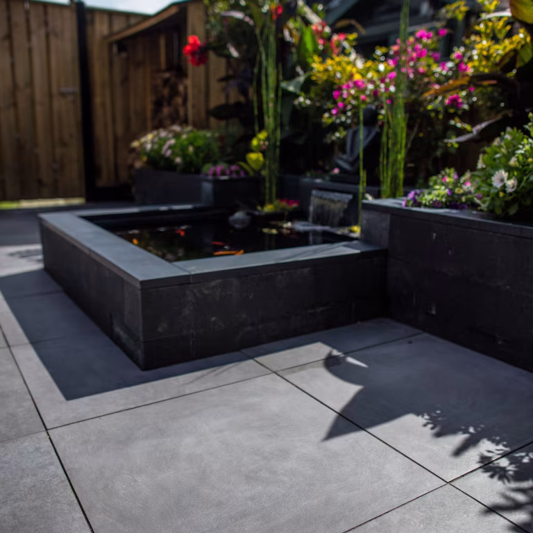 Vijver met zwarte rand op terras van GeoCeramica Fumato Mezzo met kleurrijke bloemen