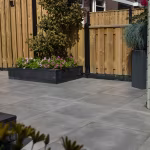GeoCeramica Fumato Mezzo terras met houten schutting, plantenbak met roze bloemen en siergras