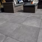 Laag gefotografeerde GeoCeramica Fumato Mezzo tegels met rieten loungeset op de achtergrond