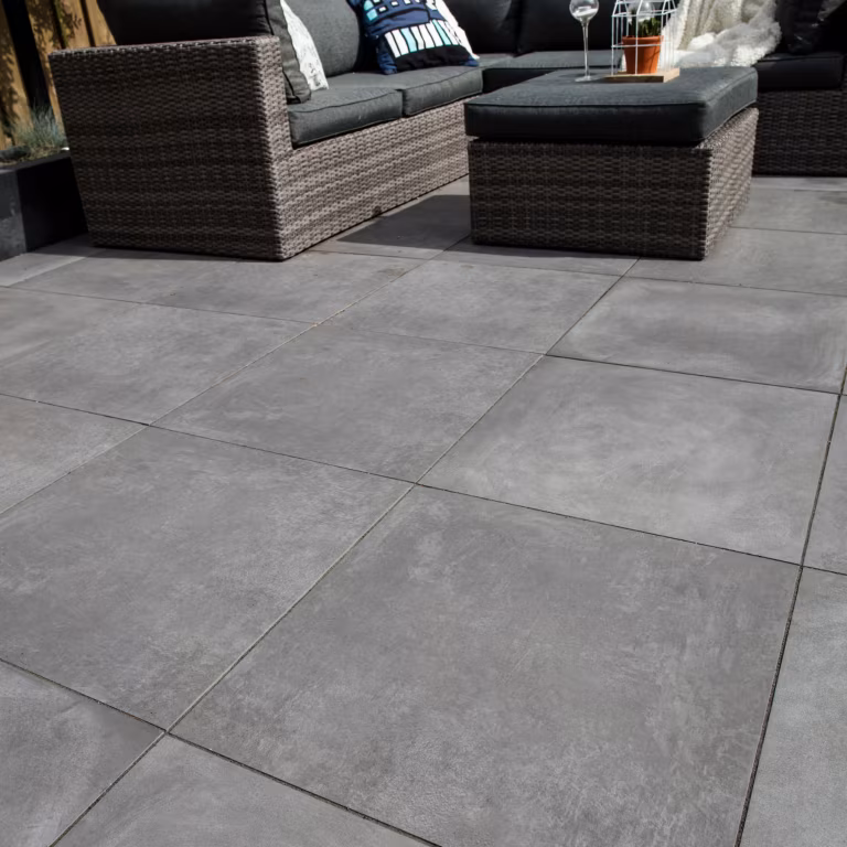 Laag gefotografeerde GeoCeramica Fumato Mezzo tegels met rieten loungeset op de achtergrond