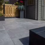 Terras met GeoCeramica Fumato Mezzo tegels voor grijs tuinhuis en houten schutting