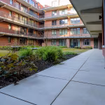 Binnentuin van appartementencomplex met pad van GeoCeramica Evoque Beige tegels langs planten