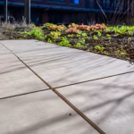Schuin close-up van GeoCeramica Evoque Beige tegels met brede voegen en plantenbed