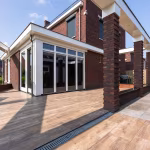Hoek van woning met witte pui, bakstenen pilaar en Timber Noce houtlooktegels met afvoergoot