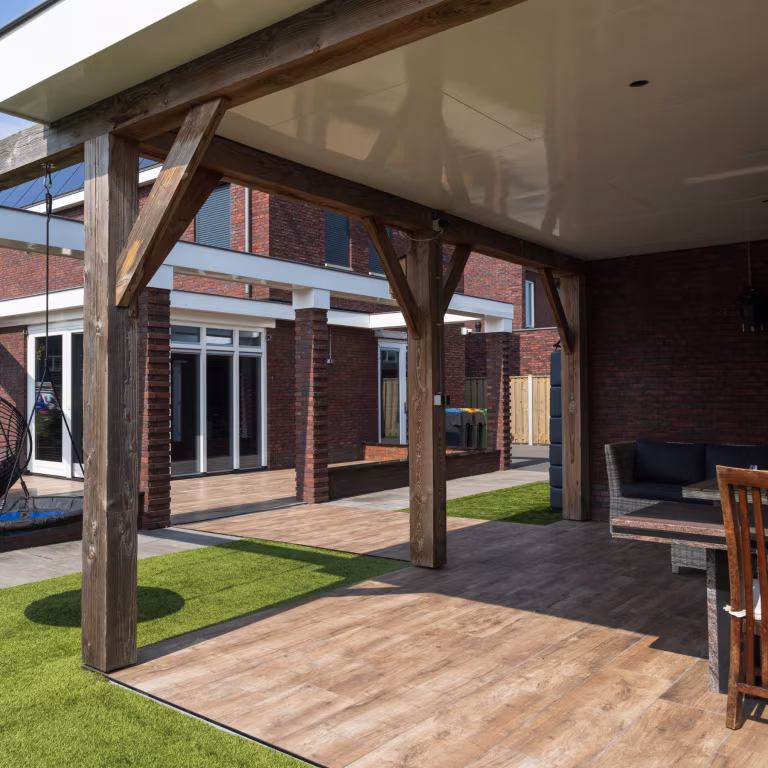 Onder overkapping uitzicht op Timber Noce terras, kunstgras en bakstenen woning met pui