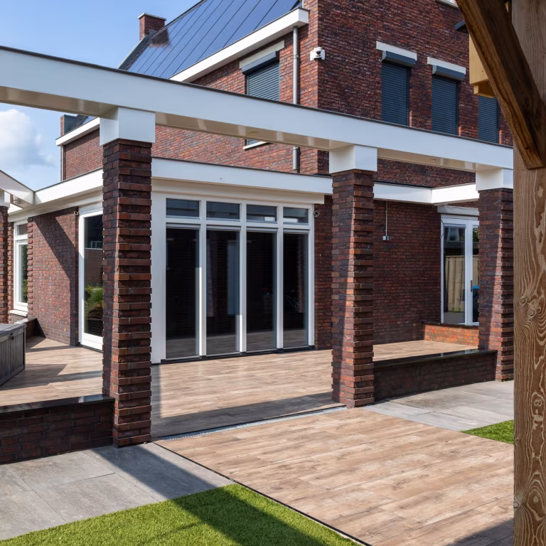 Woning met witte pui, bakstenen pilaren en terras van Timber Noce tegels op kunstgras