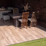 Eettafel met houten stoelen op vloer van Timber Noce houtlooktegels naast kunstgras
