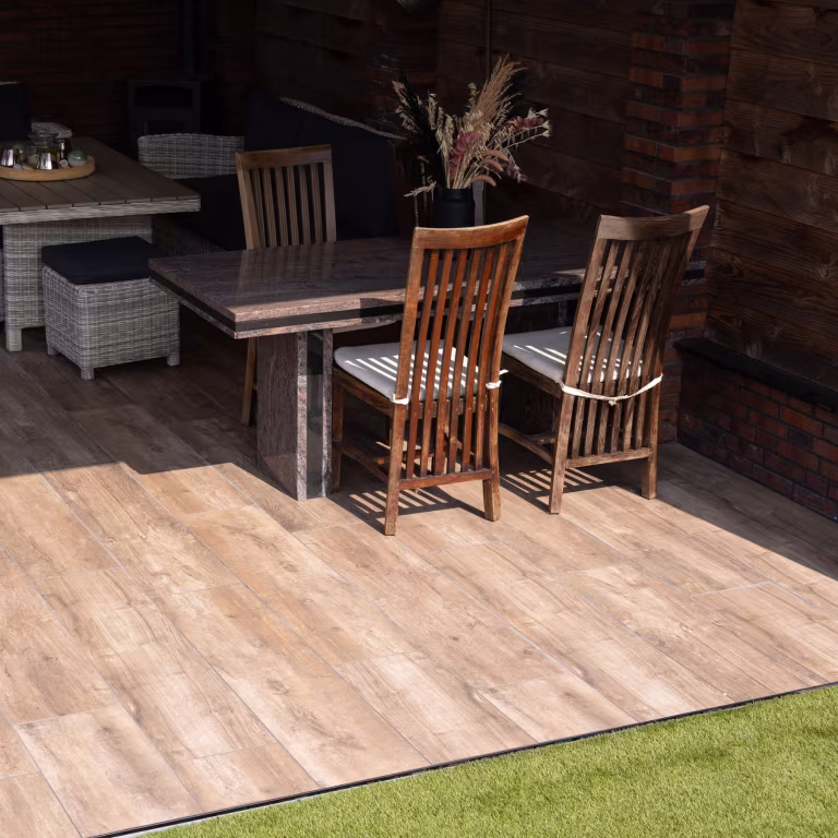 Eettafel met houten stoelen op vloer van Timber Noce houtlooktegels naast kunstgras