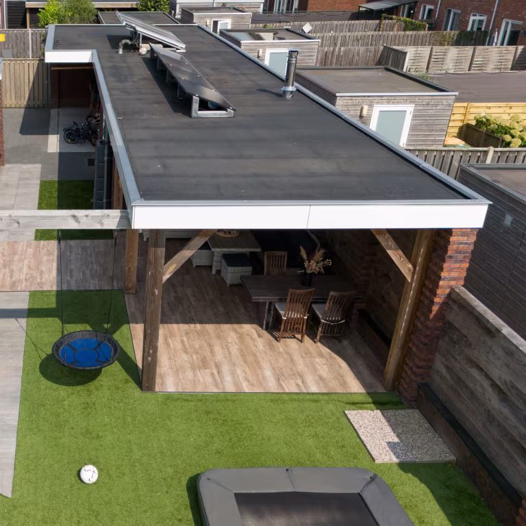 Luchtfoto van terras met Timber Noce houtlooktegels, kunstgras, trampoline en overkapping