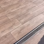 Close-up van Timber Noce houtlooktegels in verspringend patroon naast afvoergoot