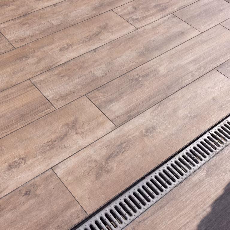 Close-up van Timber Noce houtlooktegels in verspringend patroon naast afvoergoot