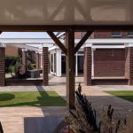 Houten balken van overkapping met sierplant voorgrond en Timber Noce terras met kunstgras