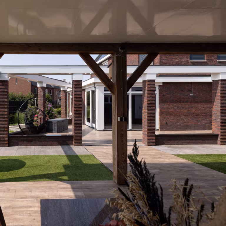 Houten balken van overkapping met sierplant voorgrond en Timber Noce terras met kunstgras