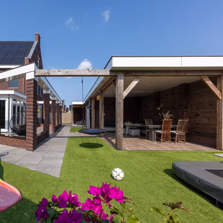 Tuin met kunstgras, voetbal en roze bloemen voor overkapping met Timber Noce vloer