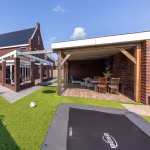 Overkapping met eettafel naast trampoline en kunstgras, vloer van Timber Noce tegels
