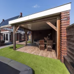 Overdekte veranda met eettafel en stoelen, vloer van Timber Noce tegels, trampoline voorgrond