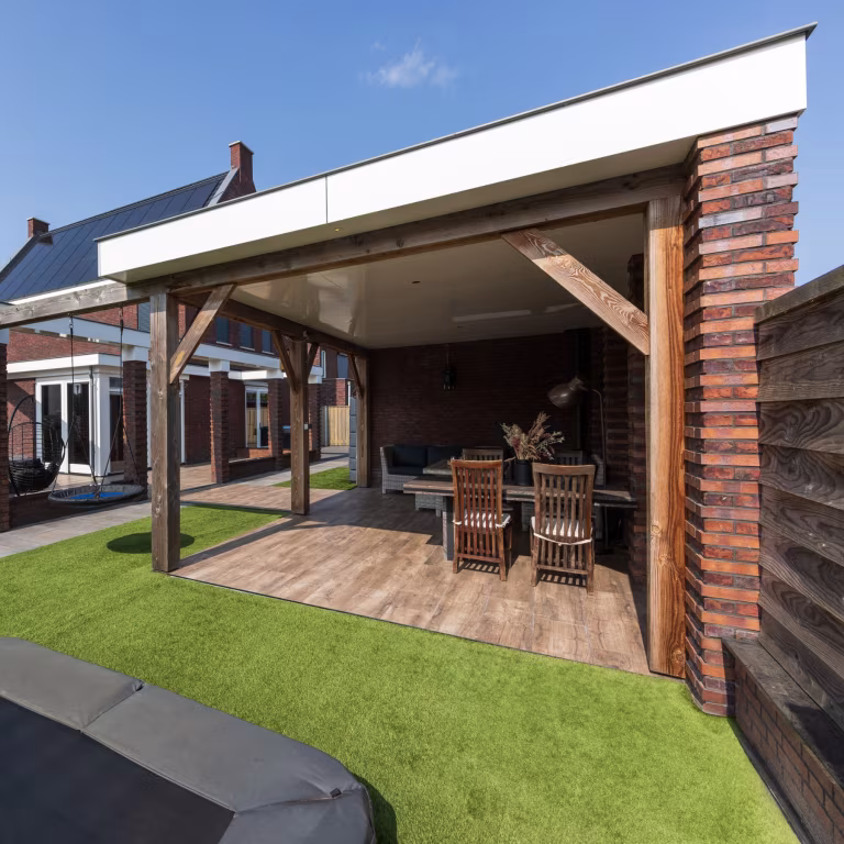 Overdekte veranda met eettafel en stoelen, vloer van Timber Noce tegels, trampoline voorgrond