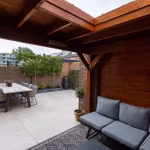 Terras met houten overkapping, loungebank en eettafel op lichte GeoCeramica 60x60 tegels