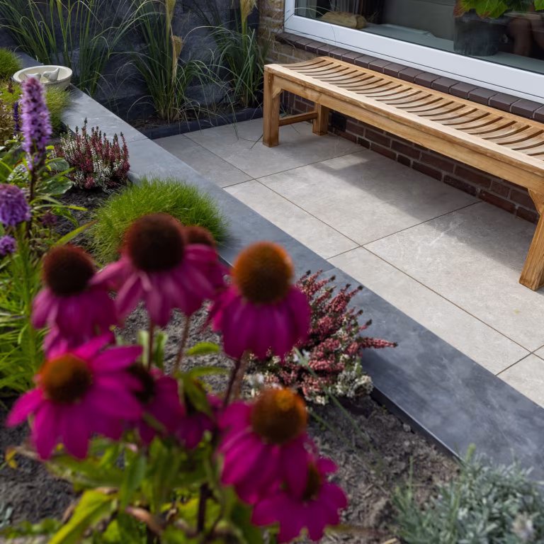 Bloeiende planten en houten bankje naast lichte GeoCeramica Palanta Plus Gold terrastegels
